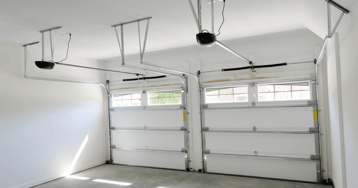 Interior view of a clean two-car garage with white sectional doors, window panels, and ceiling-mounted automatic openers