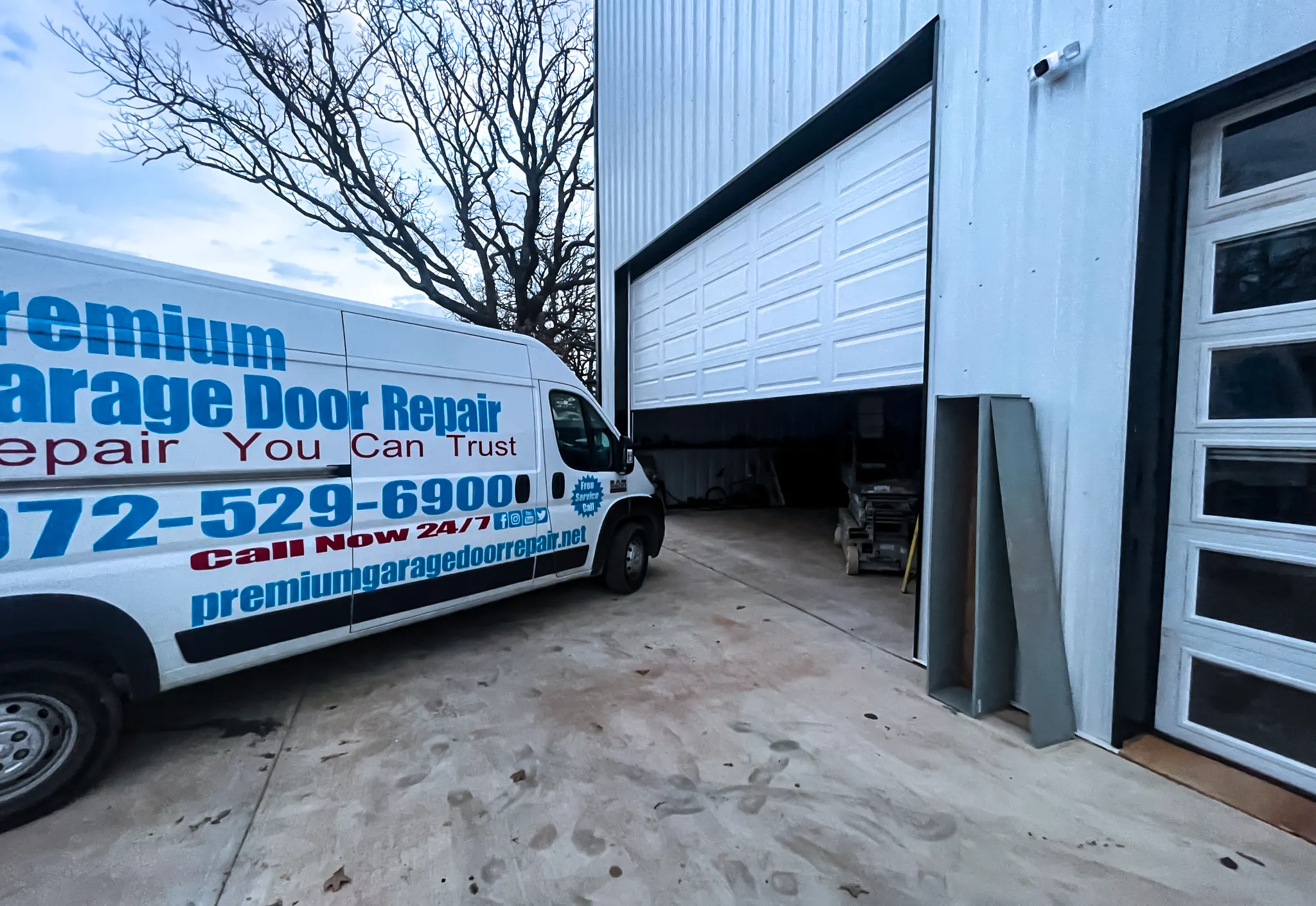 Premium Garage Door Repair branded service van parked beside a partially open white commercial garage door on a metal